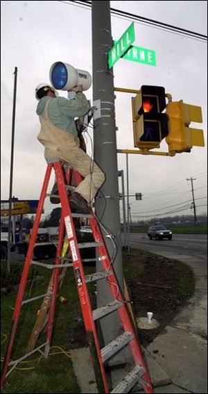 Allan Wright of ET Electric Corp. installs the strobe unit of the camera system to catch drivers who run red lights at Byrne Road and Hill Avenue.