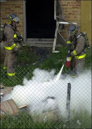 Firefighters use extinguishers to put out smoldering trash fires removed from the abandoned mental health center.