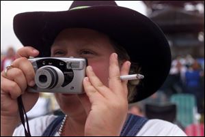 Joann Weaver of Paulding tries to photograph one of the performers while keeping her cigarette intact during the concert at the Hickory Hill Lakes campground in Fort Loramie.