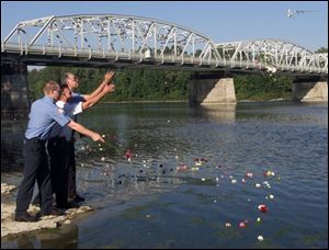 Waterville volunteer firefighters Ed Metzger, from left, Lt. Tom Hilton, and Bob Schardt throw flowers of remembrance into the Maumee River during a memorial service that was held in Waterville yesterday.