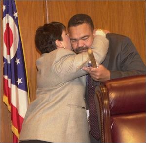 Jack Ford, at a meeting of the Lucas County commissioners, gets a hug from board President Sandy Isenberg, who presented the new mayor with a small baseball bat and brick.