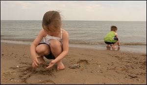 Breanna Chaffin, 4, plays in the sand while Zach Murphy, 2, hunts for stones and shells along the beach in Port Clinton.