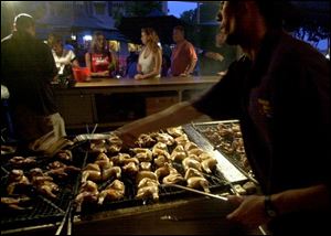 Louis Trzaska from Poland, who is working on the island for the summer, cooks chicken at the Chicken Patio to help feed visitors to the island who wait at the counter for their orders.