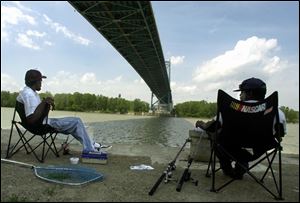 Ray Woodson, left, and Leonard Braxton, both of Toledo, relax in the shade of the Anthony Wayne Bridge while fishing in the Maumee River.