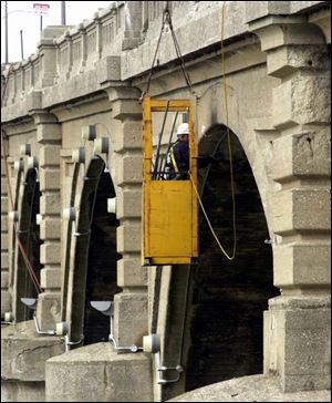 rov photo by don simmons nov 14, 2002  stan cross an employee with e t  electrical works from  a bucket that is held by  a crane on the pavement above.  he is removing the lights from the martin luther king bridge
