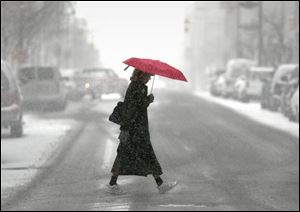 ROV redspot 01 - 120202 - A woman walks across Huron St. at Madison as shee tries to protect herself from the falling snow with a red umbrella which is a stark contrast to the newly fallen white blanket of snow downtown. The Blade/Allan Detrich