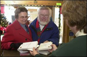 Mary and Tom Seitz, at left, often mistaken for Mr. and Mrs. Santa Claus, hand over their mail to Marsha Deitemyer, postmaster in Rudolph, for the distinctive hand-stamp that is used there during the holidays, above.