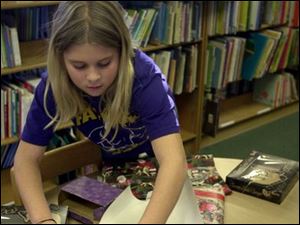 Ten year old Kaylee Ehman wraps  Christmas presents for her family at the Normal Memorial Library in Fayette,OH. She purchased the presents with library 'money' (play money she earned durng the after school childrens program at the library) and spent the money at the special gift store set up for the kids to purchase Christmas presents for themselves or  for the family. Lisa dutton REG wrapper DEC 16 2002