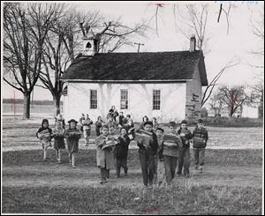 First and second grade pupils in 1950 carry school supplies from their old one-room school house in Riley Township across the field to a new school.