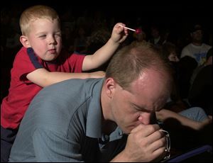 Nate Elarton, pastor of Bedford Christian Community Assembly of God, Temperance, prays at a `Heal Our Land' event as his son, Levi, 3, engages in a little mischief with his sucker. The event last night was held in conjunction with the National Day of Prayer.