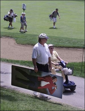 Bob Miller carries a mounted poster of Arnold Palmer for his mother, Eileen Miller, riding beside him. Their mission was to get the storied golfer's autograph on it. Mrs. Miller obtained the poster nearly 20 years ago at Sears, which used it to promote an Arnold Palmer line of clothing. Mr. Palmer doesn't sign autographs until after the 18th hole.