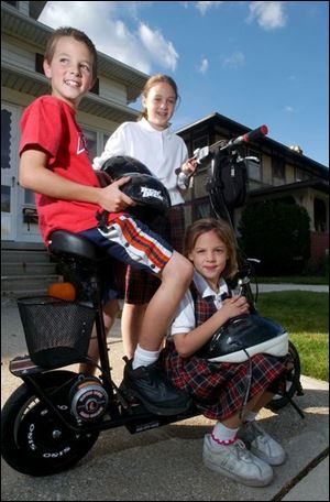 Zachary, Jackie, and Mackenzie Guenin, from left, are enthusiastic about the battery-powered scooter their dad bought a week ago to help them get around their South Toledo neighborhood efficiently. But police point out that it's illegal to ride the scooters on sidewalks. 