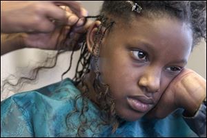 Michelle Holmes, 9, waits patiently as Lashawnda Horton braids her hair at Divas and Gents on Lagrange Street.