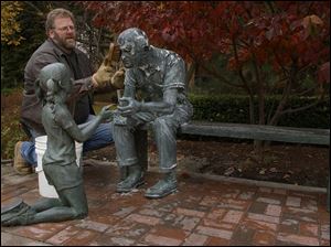 CTY GIRL06P 1 11/6/03 PHOTO BY LORI KING Ken Thompson, of Flatlanders Sculpture Supply, Blissfield, MI, gives the old man in the Seasons sculpture a bath while the little girl watches. The man and girl were reunited after she was vandelized and taken away to be fixed.