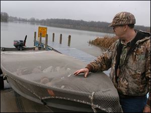 Rov Raymond Lay, of Monroe Mich,  checks the tiedown netting on his boat,   which he says is his own inovation  -  at Halfway creek access site.  - It does not flap  like canvas -  he just pulled in from duck hunting, note decoys in boat.  he says he did not get a shot off. blade photo  by herral long  11/17/2003