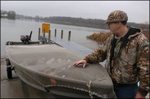 Rov Raymond Lay, of Monroe Mich,  checks the tiedown netting on his boat,   which he says is his own inovation  -  at Halfway creek access site.  - It does not flap  like canvas -  he just pulled in from duck hunting, note decoys in boat.  he says he did not get a shot off. blade photo  by herral long  11/17/2003