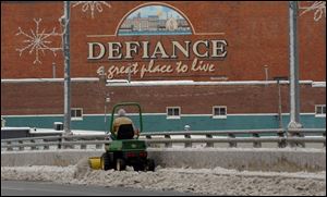 A county worker clears snow and ice from the sidewalk over the bridge on Clinton Street in Defiance.