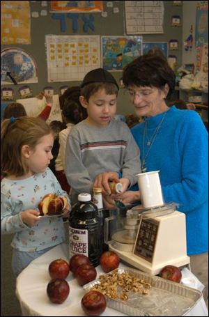 Jolie Brochin, 5, holds sliced apple as Matthew Fink, 5, and Phyllis Wittenberg put spice into a food processor.