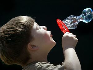 ROV bubbles 01 - Kenny Spence, 6, blows bubbles in the bright sun of a spring day that is finally fit for short shirt sleves, under the watchful eye of his mother Tammy, on lincoln St. in Findlay. Allan Detrich/The Blade