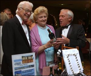 ILLUMINATING TIME: From left, Frazier, and Susan Reams discuss a bottle of wine that's up for silent auction with Mike Robarge during the Illuminations benefit at the Franciscan center.