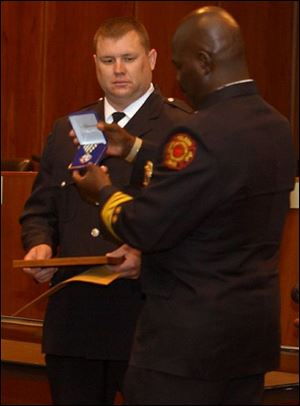 Toledo firefighter Scott Hathaway receives a Medal of Commendation from Fire Chief Mike Bell.