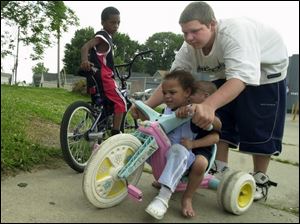 Monte Miller, 8, watches as Corey Corbin helps steer Heaven Baker, 3, and her brother, B.J., 2, near their homes on Broadway in South Toledo. Corey, 14, was keeping tabs on the younger kids yesterday as they played outside. Children may be confined to indoor play today, as forecasters are calling for rain.