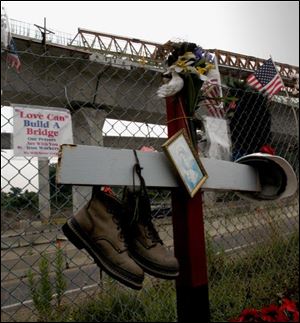 A pair of sturdy work shoes, a hard hat, and a small print of the Madonna and Child complement a makeshift cross erected at the site to remember the workers killed and those injured.