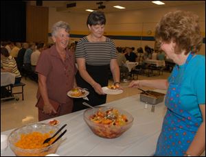 Just as students will do next week, Barb Contat, a teacher from Monroe, and Cathy Griffith, Ida High School principal, receive breakfast fruit from cook Vivian Gross at Ida High School.