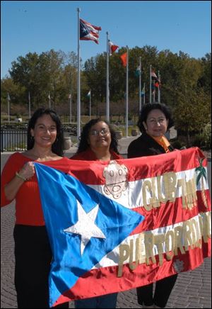 Carmen Vega, Gladys Flores, and Maria Gonzalez hold their club flag in front of the Puerto Rican flag that flies atop a 20-foot pole at International Park.