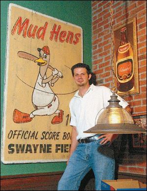 Eric Barker stands next to a Mud Hens wall hanging that his team of artists made to look like a vintage piece.