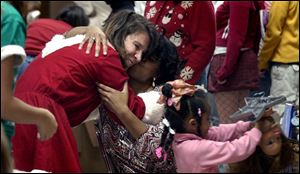 Joni Meyer-Crothers, left, accepts a hug from Tabatha Thomas as daughter Janet, 4, enjoys one of her gifts. Mrs. Meyer-Crothers and her family give the party to honor her late mother. 