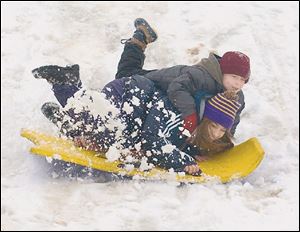 Maumee residents Nicole Figueroa, 14, and Devin Fox, 7, share a ride down an incline at Indian Hills Park. Much of the snow could melt today, as temperatures are expected to reach the middle to upper 50s. 