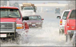 Vehicles slosh through water covering U.S. 20 west of Fremont yesterday.