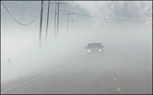A vehicle makes its way down Salisbury Road in Monclova Township through a thick blanket of fog.
