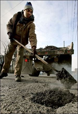 Rayford Sturdevant, a Toledo street worker, fills some of the many potholes in Front Street with patching material.