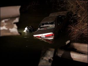 CTY accident15p 1 A diver hooks chains to a car that went through a guard rail , in foreground, on Alexis Road Tuesday, 03/15/05, in Toledo, O. The car crashed into a creek. The Blade/Jeremy Wadsworth