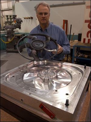 Weaver Tool president Robert Weaver holds a prototype fan blade that could be used in the auto industry. The mold for making the part is in the foreground.