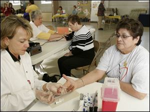 NBR health09p Sally Hogrefe, left, a cholesterol screener from The Fulton County Health Center, gets a blood sample from Elvira Rodriguez of Delta, during a free health fair at Our Lady of Mercy Church in Fayette, O., on Saturday, 4/9/05.  Sharon Gericke, an LPN with the Fulton County Health Center, checks the  blood pressure of Glenda Rupp of Fayette, in background.  The Blade/Dave Zapotosky