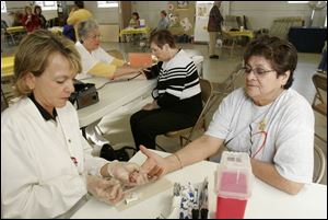 NBR health09p Sally Hogrefe, left, a cholesterol screener from The Fulton County Health Center, gets a blood sample from Elvira Rodriguez of Delta, during a free health fair at Our Lady of Mercy Church in Fayette, O., on Saturday, 4/9/05.  Sharon Gericke, an LPN with the Fulton County Health Center, checks the  blood pressure of Glenda Rupp of Fayette, in background.  The Blade/Dave Zapotosky