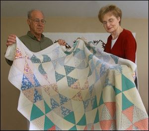 Howard and Carolyn Snyder hold up one of the 18 quilts in their Pettisville home. 