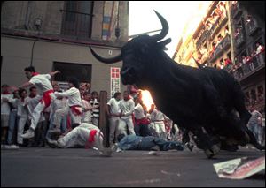 A bull makes a turn around a corner as runners scramble to get out of the way during Pamplona's Running of the Bulls.