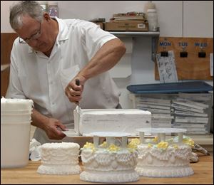 Dennis Wixey spreads the first of two coatings of frosting on the base of the cake. The three tiers in the foreground are completed.