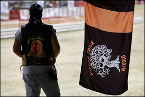Richard Pontious, wearing a leather vest with a drawing of the Vietnam veterans memorial, watches the band at the Veterans Bash in Promenade Park. Nearby is an Agent Orange flag.