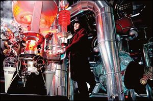 Johnny Depp plays the eccentric candymaker Willy Wonka in his factory wearing a top hat, velvet coat, and a large smile.
