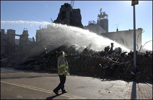 Firefighter Brian Schoen looks on as Unit No. 7 of the Toledo Fire Department sprays water on the remains of burned building at Monroe and Ontario. Thursday s fire, which devoured the historic four-story commercial structure, kept fire crews battling for hours, and sent a huge plume of smoke wafting over the downtown skyline. The suspicious blaze has led to a call for the city to consider enacting an ordinance on how long buildings can sit vacant.