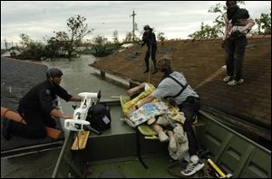 New Orleans police officers maneuver a rescue boat between the roofs of flooded houses in the city's hard-hit Ninth Ward as Times Picayune reporter Alex Brandon, right of boat, holds onto a hurricane victim.
