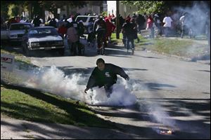 A protester tries to pick up a tear gas canister that was shot in his direction at Mulberry Street and Central Avenue as others run away from police officers during the daylong melee.