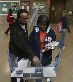 Elections board worker Hugh Ross shows UT student Cherron Carter, 18, a first-time voter, how to use the new voting machine at the University of Toledo's Scott Park campus.