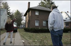 The mother of 'Stacy' points to the house where her daughter and niece 'Cara' were held, while Cara's father looks on.