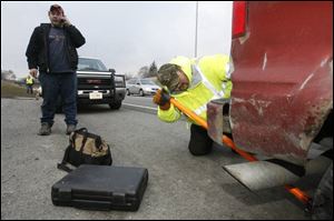 ODOT highway technician Brian Amos positions a jack under the rear of Joseph Riggs' disabled van, as Mr. Riggs calls a relative to explain he has help on the scene along I-475 at Central Avenue.
